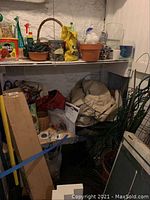 View of garden supplies including terra cotta pot, vases, bags, and garden stakes on shelves and floor.