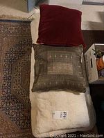 Three cushions laid out: large white fluffy cushion at bottom, smaller brown patterned cushion, and red velvet cushion on top.