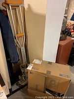 Pair of aluminum crutches leaning against wall next to boxed Toto Washlet