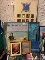 Framed prints and pictures stacked against a wall, featuring impressionism themed prints and various sizes