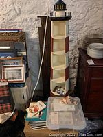 Full view of wooden lighthouse-shaped shelf, approximately 55 inches tall with coat hooks, with shell collection books and assorted papers on and around it.