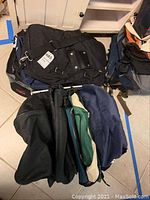 Top view of multiple backpacks and gym bags in black, blue, green and other colors stacked together