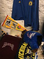 Harvard fleece blanket, University of Michigan pennant and plush toy in sports jersey shown along with a Boston Marathon jacket