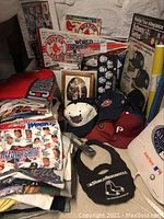 Photo showing folded All-Star Game t-shirts, multiple baseball hats, framed photos and memorabilia, and 1986 Boston Red Sox World Series signage