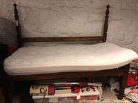 Front view of the day bed with mattress in place, showing the wooden frame and turned posts against a stone wall.