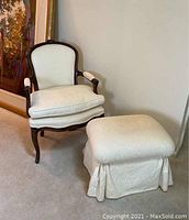 White damask upholstered accent armchair and ottoman placed side by side near a wall, showing full view of the chair's carved wood frame and padded cushions.