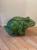Side view of the green ceramic frog garden stool showing textured features and glossy glaze.