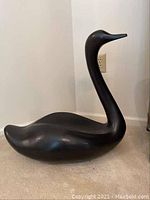 Full side view of the smooth black swan sculpture showing overall shape and size in relation to outlet on the wall