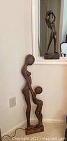 Carved wood mother and child sculpture leaning against corner