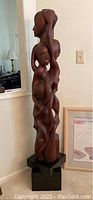 Full front view of the 65" tall wooden sculpture on black pedestal