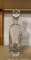 Full front view of clear crystal decanter with stopper on wooden shelf