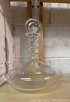 Front-facing view of decanter and stopper on wooden shelf against masonry wall