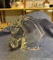 Front-side angle view of clear Baccarat crystal horse bust on blue-gray fabric showing detailed mane and contours.