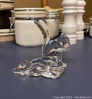 Clear Baccarat crystal squirrel figurine depicted standing upright with curved tail, shown on a dark blue surface with kitchen items in the background.