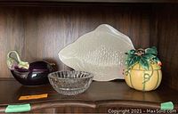 Full lot showing four items on wooden shelf: purple eggplant server, two crystal ashtrays, cream fish platter, and pumpkin container.