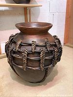 Full view of tall decorative brown pot with wicker wrapping, showing form and placement of wicker braids.
