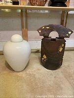 Wide shot showing both the white Murano glass vase and the signed metal sculpture side by side on the floor.