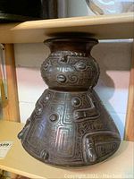 Front and side angled views of a tall etched vase with detailed geometric and figurative raised elements.