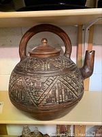 Full front view of the large clay garden teapot showing rounded etched designs, large handle, and repaired spout.