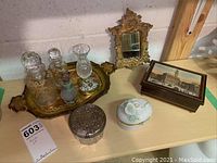 Group photo showing all lot items on a table against a wall including perfume bottles on a tray, trinket boxes, mirror, and music box