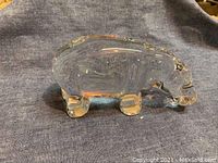 Side view of clear Baccarat crystal hippopotamus figurine placed on a dark cloth background showing smooth, rounded crystal body and short legs.