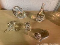 Group photo showing all five clear crystal animal figurines: a small bear, a walrus, a seal, a goose, and a gander on a wooden surface.