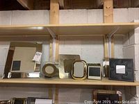 Top shelf showing a variety of picture frames including large mirrored rectangular, round ceramic, small gold and black metal frames, and black leather stitched frame.