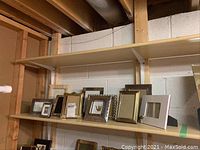 Left half of top shelf showing a row of various picture frames ranging from small to medium sizes including metal, ceramic, and fabric frames.