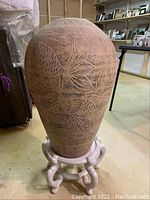 Full view of the etched clay vase on the wooden pedestal, showing fish and aquatic plant designs.