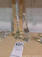 Two clear crystal figurines, a giraffe and a cat, shown together on a wooden surface with a lot number card.