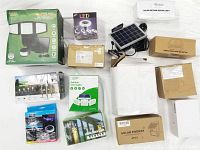 Multiple boxed solar lights including floodlights, fence lights, and garden stakes arranged on a white backdrop