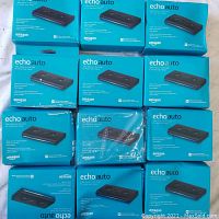 Photo of twelve Amazon Echo Auto devices in turquoise packaging, some sealed and one in plastic wrap.