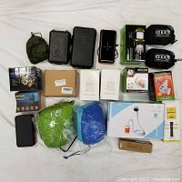 Overview photo showing the full lot including boxed light products, mesh pillows, hammock suspension systems, mosquito light repellent, small black cases, and other camping gear arranged on a white surface.