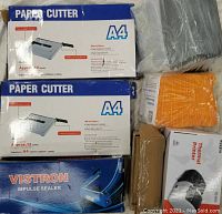 Two boxed A4 paper cutters, sealed impulse sealer box, thermal printer box, bubble envelopes and other boxed items viewed together.