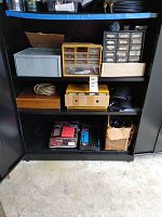 Full view of black metal cabinet shelf with multiple organizer units, boxes, rope, knee pads, and tool kits inside.