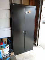 Full front view of a tall black metal locking cabinet with two doors in a storage or garage environment.
