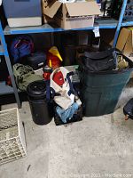Wide view showing camping gear items on floor by shelving including lantern, gas can, backpacks, tent, and containers