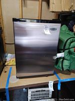 Front view of stainless steel mini fridge with black top trim showing SPT brand and visible scratches.