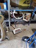 Floor cleaning head attachment with upright metal handle attached to a hose scrunched on the floor.
