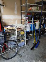 Photo of wire shelving units containing brooms, cleaning supplies, and some cloths in a garage or workshop setting.