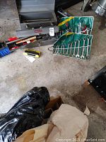 Overview of household tools on concrete floor including green roll-up wrenches, metal toolbox, hand tools, socket sets, and shelf hardware