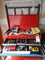 Opened red Craftsman metal toolbox showing top compartment with assorted hand tools and accessories including tape measure, zip ties, paint can openers.