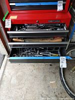 Red Craftsman tool chest with multiple drawers open showing various hand tools inside.