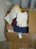 Box of assorted kitchen and bathroom linens showing different folded towels and cloths in various colors and fabrics.