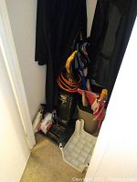 Photo of closet showing Hoover vacuum with orange cord, hanging men's coats, yoga mat, umbrellas, and bags at base