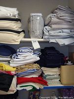 View of shelves with three main shelves filled with folded linens including bed sheets, towels, curtains, and hand towels in various colors and sizes.