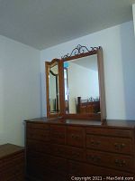 Front view of large dresser with tri-fold mirror and decorative metal scrollwork on top, showing drawer fronts and handles.