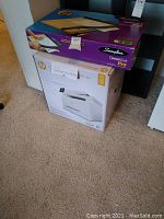 Both boxed HP printer and Swingline trimmer stacked on carpet
