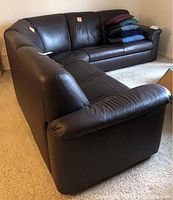 L-shaped configuration of dark brown leather sectional shown from side angle with cushions and pillows on the seats.