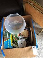Photo of open box with various kitchen items inside including containers, scale, and crocheted hot pads.